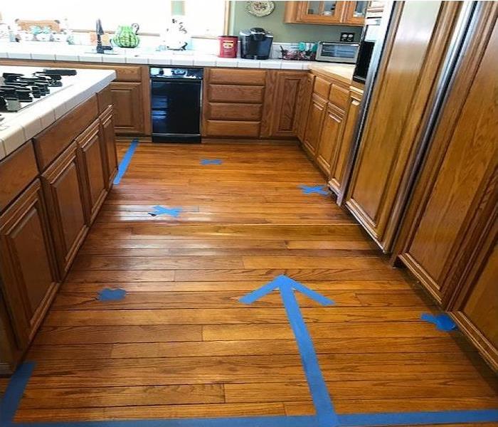 Wood flooring of a kitchen with blue tape marking the affected areas. 