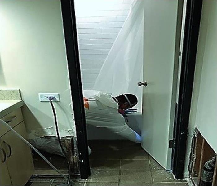 Technician on his hands and knees cleaning a sewage backup with PPE