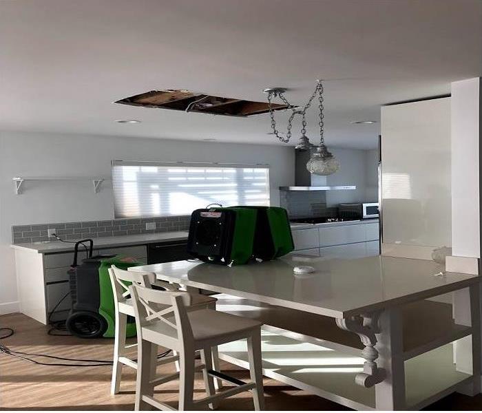 A modern kitchen with light brown wood flooring and a marble table with a hole in the ceiling.  