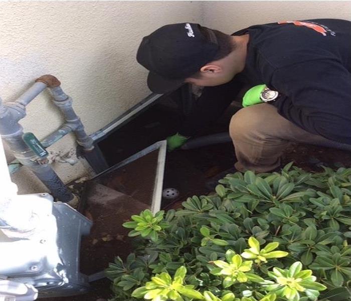 Crew member with a hose kneeling by a crawlspace entrance extracting water