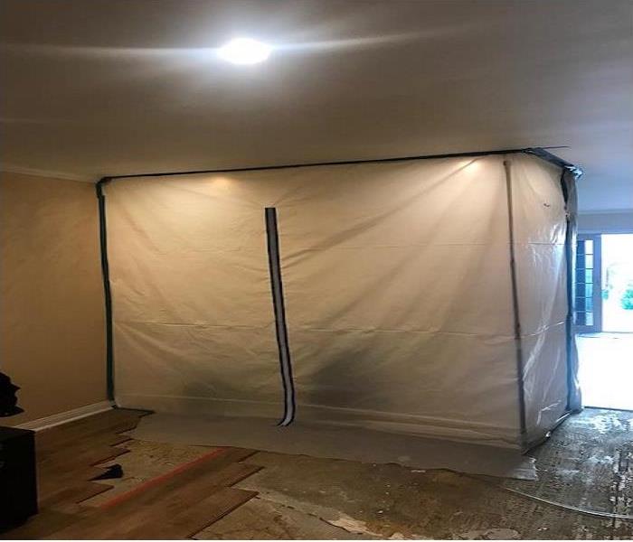 A containment of heavy duty plastic and blue tape surrounding an open wall that is being prepared for abatement.
