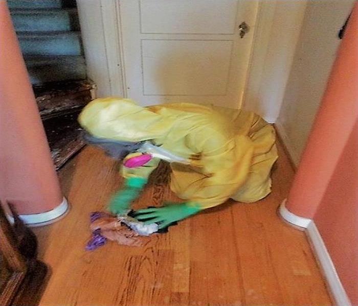 Technician with a yellow PPE and respiratory mask cleaning the floor or a crime scene.